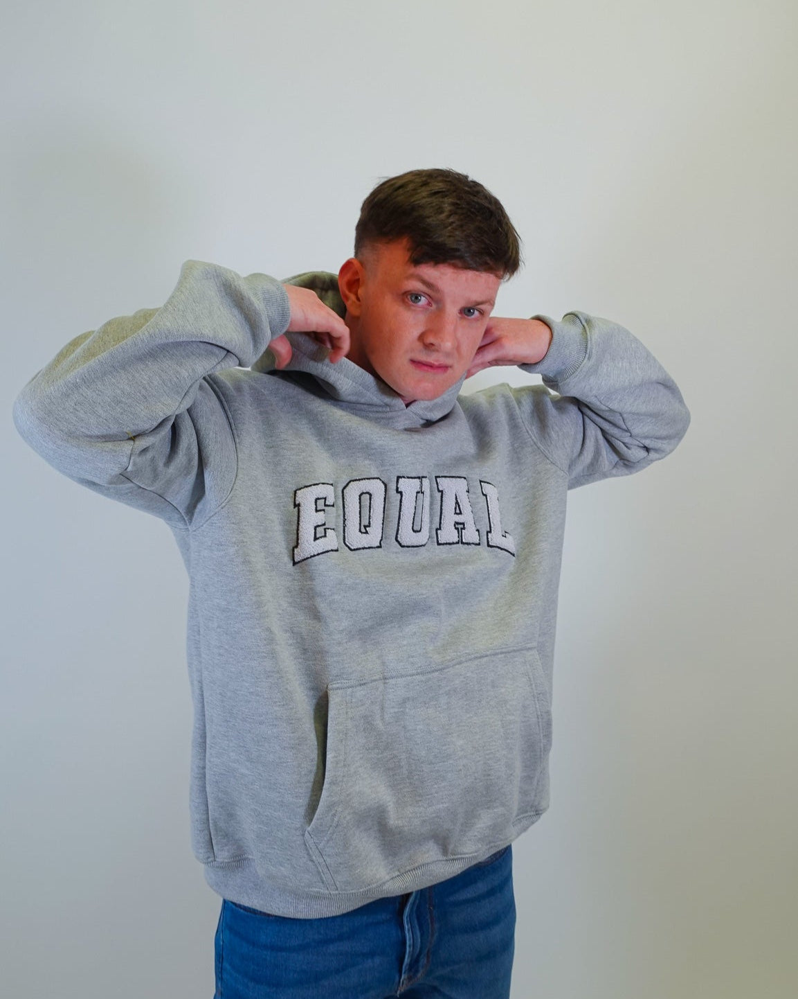 Person wearing a gray hoodie with 'EQUAL' text on a plain background