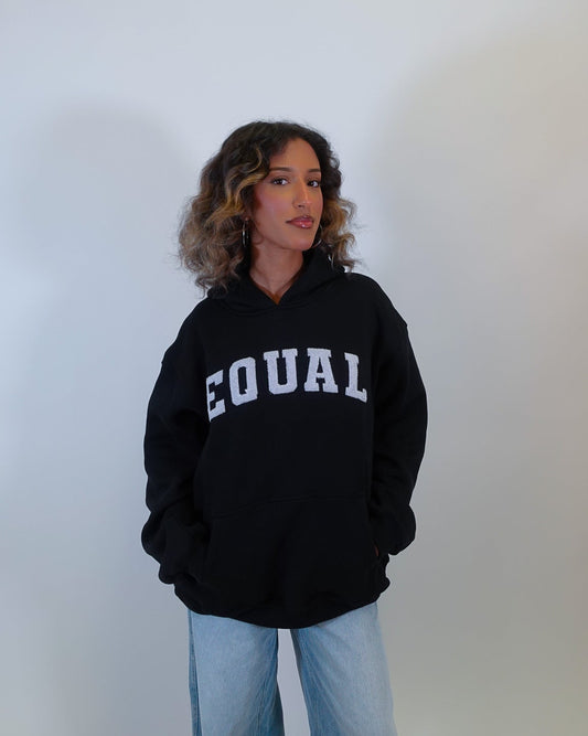 Person wearing a black hoodie with 'EQUAL' text on a plain background